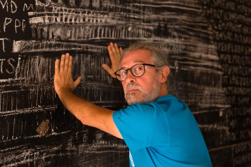 Fotografo artisti Giorgio Sacher - artista con-maglietta azzurra appoggiato con le mani alla lavagna